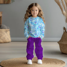 Laden Sie das Bild in den Galerie-Viewer, Baumwolljersey Blütenzauber Eisblau – Zarte blau-violette Blüten auf einem hellblauen Hintergrund mit feinen Lichtpunkten. Kleidungs-Mockup: Kleines Mädchen im Langarmshirt.