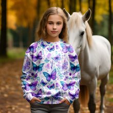 Laden Sie das Bild in den Galerie-Viewer, Baumwolljersey Schmetterlingswiese Pastell – Schmetterlinge in Türkis und Violett zwischen zarten Blüten auf hellem Grund. Kleidungs-Mockup: Mädchen im Langarmshirt neben weißem Pferd.