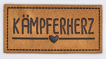 Laden Sie das Bild in den Galerie-Viewer, Detailaufnahme eines geprägten Kunstlederlabels „Kämpferherz“ für Hoodies, Taschen und selbstgenähte Accessoires.