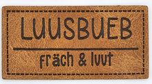 Laden Sie das Bild in den Galerie-Viewer, Detailaufnahme eines geprägten Kunstlederlabels „Luusbueb – fräch & luut“ in Schweizerdeutsch für selbstgenähte Kleidung und Accessoires.