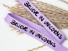 Laden Sie das Bild in den Galerie-Viewer, Baumwoll-Webband „Believe in Unicorns“, 12 mm breit – flieder mit schwarzem schriftzug, Ansicht des Spruchbands.
