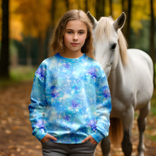 Laden Sie das Bild in den Galerie-Viewer, Baumwolljersey Blütenzauber Eisblau – Zarte blau-violette Blüten auf einem hellblauen Hintergrund mit feinen Lichtpunkten. Kleidungs-Mockup: Mädchen im Langarmshirt neben weißem Pferd.
