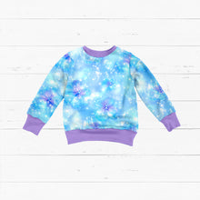 Laden Sie das Bild in den Galerie-Viewer, Baumwolljersey Blütenzauber Eisblau – Zarte blau-violette Blüten auf einem hellblauen Hintergrund mit feinen Lichtpunkten. Kleidungs-Mockup: Flach ausgelegter Pullover.
