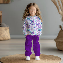 Laden Sie das Bild in den Galerie-Viewer, Baumwolljersey Schmetterlingswiese Pastell – Schmetterlinge in Türkis und Violett zwischen zarten Blüten auf hellem Grund. Kleidungs-Mockup: Kleines Mädchen im Langarmshirt.
