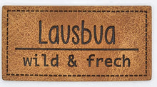Laden Sie das Bild in den Galerie-Viewer, Detailaufnahme eines geprägten Kunstlederlabels „Lausbua – wild &amp; frech“ in bayrischer Mundart für selbstgenähte Kleidung und Accessoires.
