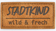 Laden Sie das Bild in den Galerie-Viewer, Detailaufnahme eines geprägten Kunstlederlabels „Stadtkind – wild &amp; frech“ für Hoodies, Taschen und selbstgenähte Accessoires.
