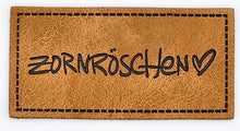Laden Sie das Bild in den Galerie-Viewer, Detailaufnahme eines geprägten Kunstlederlabels „Zornröschen“ für Hoodies, Taschen und selbstgenähte Accessoires.

